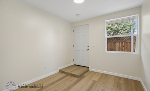 A room with a white door and a window showing a wooden fence and greenery outside.